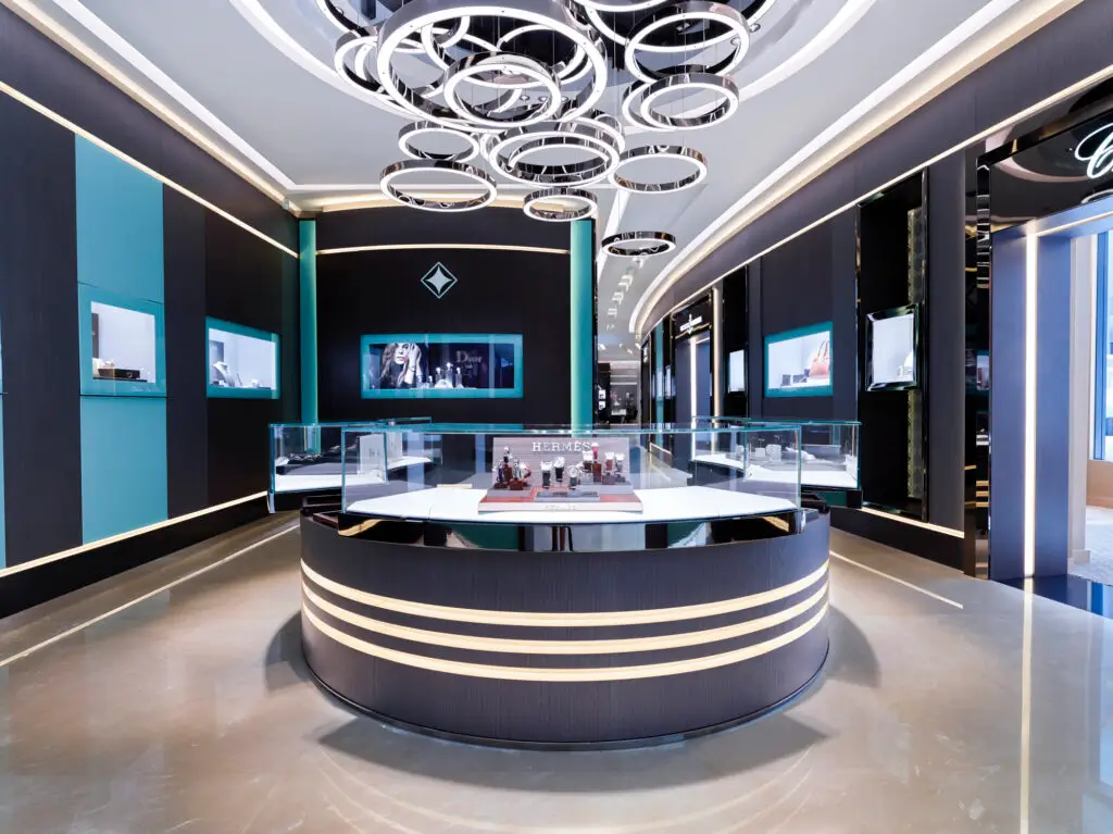 Internationales Luxus-Lichtdesign von OZ Lighting im High-End Flagship-Showroom von Ahmed Seddiqi & Sons in Dubai. Mehrere ineinander verschlungene, kreisförmige LED-Ringleuchten an der Decke kombinieren sich mit präzisen Einbauspots, um exklusive Uhren- und Schmuckvitrinen von Hermes und Chopard reflexionsfrei und brillant auszuleuchten.