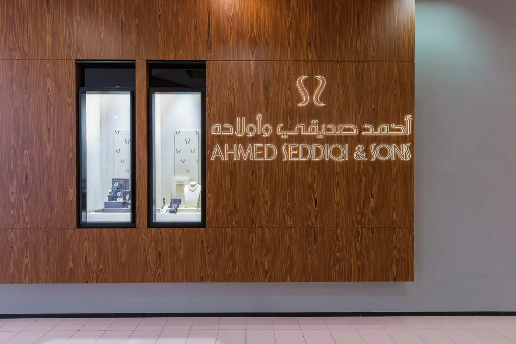 Hochwertige Fassaden- und Schaufensterbeleuchtung von OZ Lighting für Ahmed Seddiqi & Sons in Dubai. Exakt fokussierte LED-Mini-Spots illuminieren die in edle Echtholzpaneele eingelassenen Luxus-Wandvitrinen schattenfrei, während die filigrane Hintergrundbeleuchtung des Logos in Englisch und Arabisch für maximale Fernwirkung sorgt.