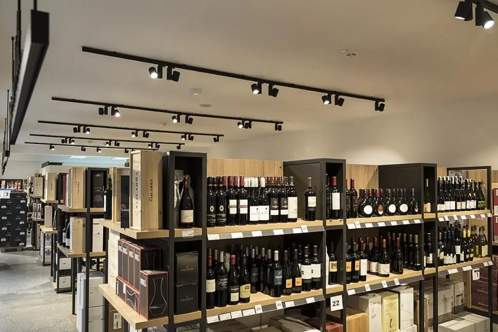 Professionelle Ladenbeleuchtung von OZ Lighting bei Wein und Feine Kost Viehbeck. Schwarze 3-Phasen-Stromschienen mit modernen LED-Spotlights setzen exklusive Weinregale durch präzise Akzentbeleuchtung und hohen Farbwiedergabeindex (CRI) perfekt in Szene.