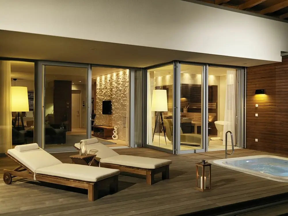Exklusive Außen- und Wellnessbeleuchtung der Geinberg 5 Spa Villas engineered by OZ Lighting. Warmweißes Architekturlicht illuminiert eine Natursteinwand, während großformatige Design-Stehlampen und Decken-Einbauspots eine luxuriöse Pool-Terrassen-Atmosphäre bei Nacht schaffen.