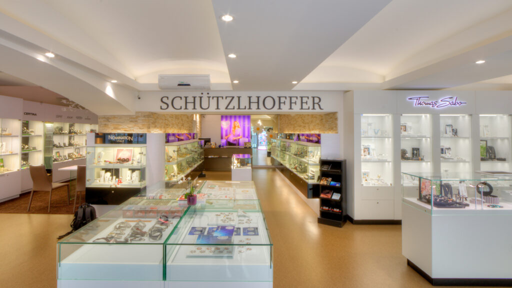 Moderne und helle Verkaufsraumbeleuchtung von OZ Lighting im Schützlhofer Trendstore in Villach. In die geschwungene Trockenbaudecke integrierte LED-Einbaustrahler sorgen für eine schattenfreie Grundbeleuchtung, während spezialisierte Vitrinenbeleuchtung die Schmuck-Displays von Thomas Sabo und Nomination reflexionsfrei und brillant illuminiert.