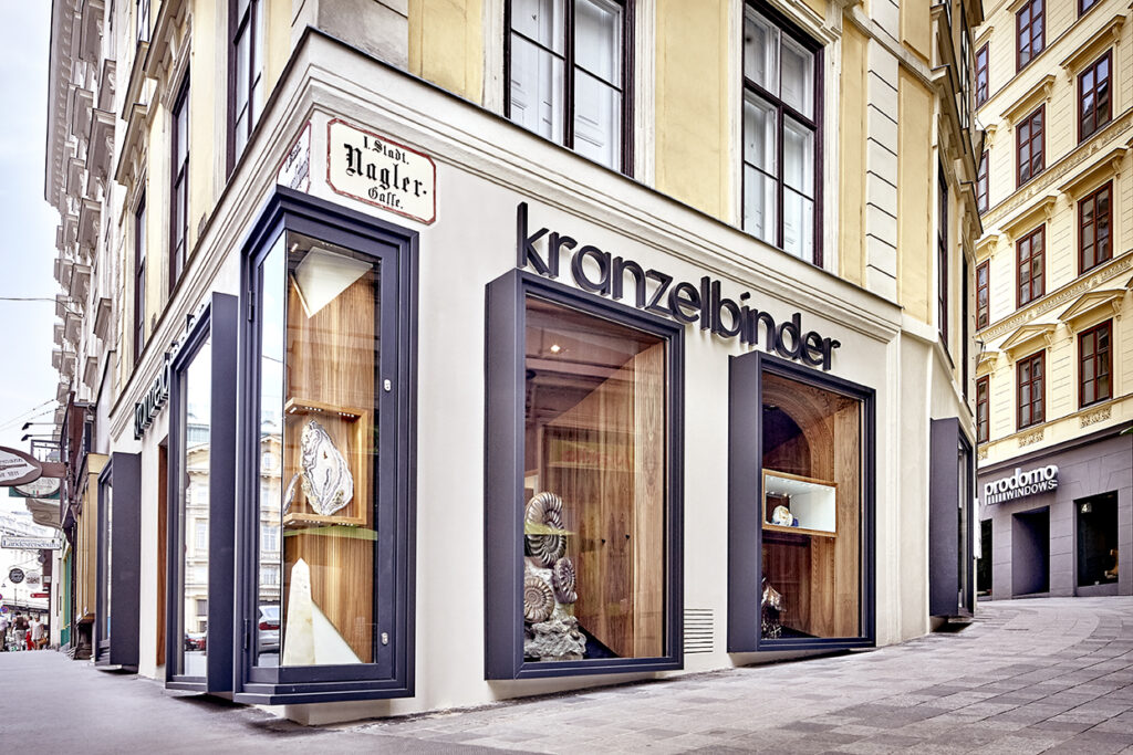 Hochwertige Schaufenster- und Fassadenbeleuchtung von OZ Lighting für den Juwelier Kranzelbinder in der Naglergasse, Wien. Leistungsstarke, tageslichtweiße LED-Architekturspots in den markanten, anthrazitfarbenen Fensterrahmen inszenieren riesige prähistorische Fossilien, Kristalle und Edelsteine vor edlen Holzwänden mit maximaler Brillanz und reflexionsfreier Ausleuchtung.