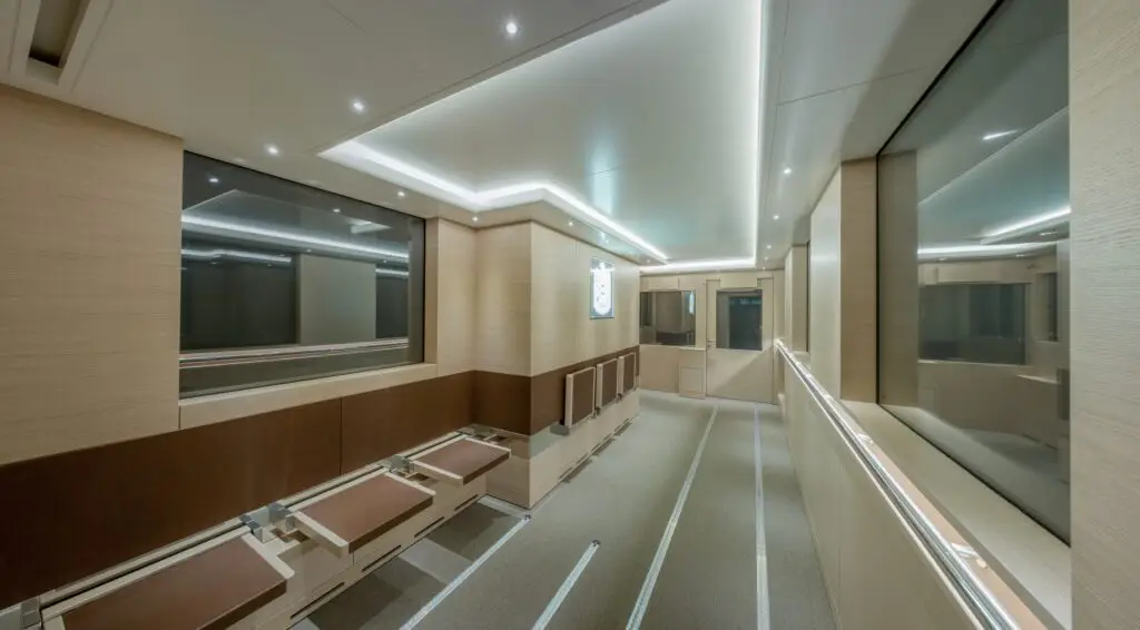 Exklusive Innenbeleuchtung und Lichtplanung von OZ Lighting in einem maßgeschneiderten Schabus VIP-Lounge-Container für internationale Staatsgäste. Die architektonische Deckenbeleuchtung kombiniert flächenbündige, lineare LED-Lichtbänder (Lichtvouten) mit minimalistischen Einbauspots für eine blendfreie, homogene Ausleuchtung der Premium-Holzpaneele und Lederbestuhlung.